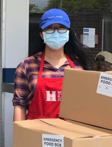 NYH employee in apron standing with emergency food box donations