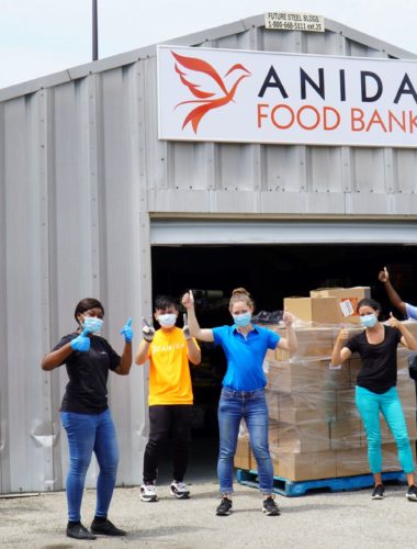 Team smiling in front of Anida Food Bank warehouse with sign