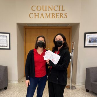 Two NYH staff standing outside Toronto Council Chambers, holding letters that community members have written to their elected official.