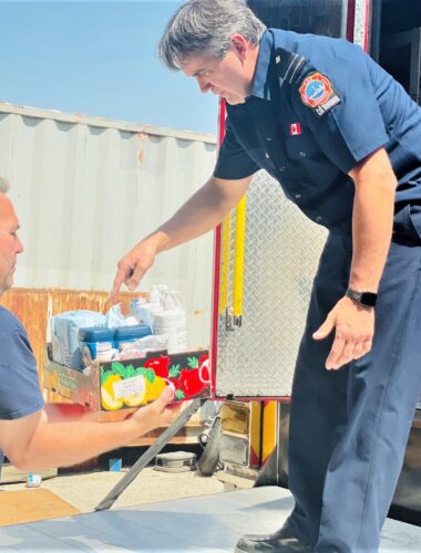 One firefighter passes a box of donated food to another as they unload food from their truck.
