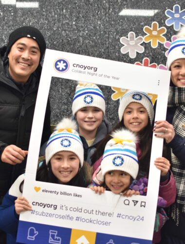 Three adults and two children hold a frame that says 'CNOY' while the childrens' faces poke out of the frame while they pose for a picture.