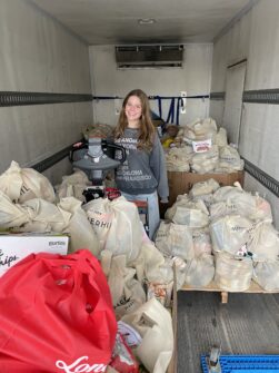 A teenaged girl stands in a truck surrounded by boxes full of donated food items as part of a food drive.