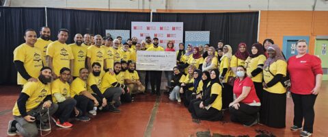 A large group of individuals wearing yellow ISV volunteer shirts and red North York Harvest Food Bank shirts stand around a large cheque for $25,000 donated to NYH.