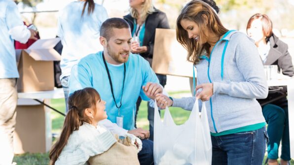 A mother, father and daughter kneel on the grass packing food donations into a bag