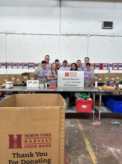 Volunteers from Jazwares stand in a warehouse with a North York Harvest Food Bank sign that says how much food they sorted for their community.