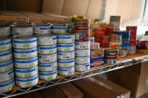 Rows of canned tuna and canned meat sit on a shelf at a food bank.