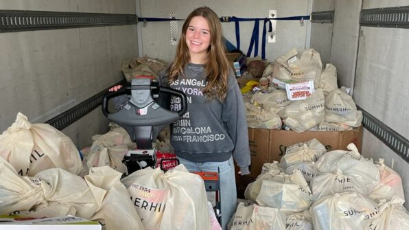 A teenaged girl stands in a delivery truck full of bags of food donations.