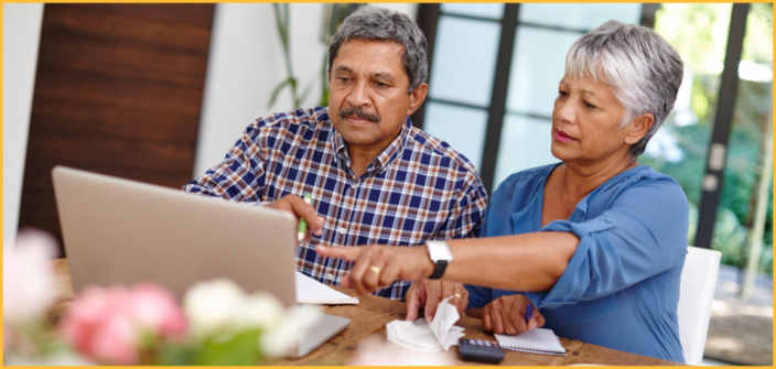An older couple sit in front of a laptop, pointing at something on the screen.