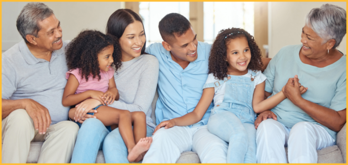 An intergenerational family of six sits on a couch smiling and laughing 
