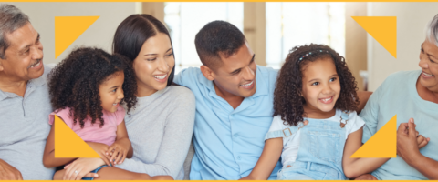 A family of six are sitting close together, laughing and smiling with their two young children.