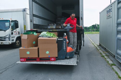 A man with skids of food lowers them from the back of a delivery truck in a parking lot.