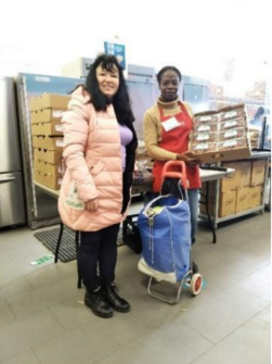 A woman stands with an employee at a food bank who is wearing a red North York Harvest Food Bank apron.