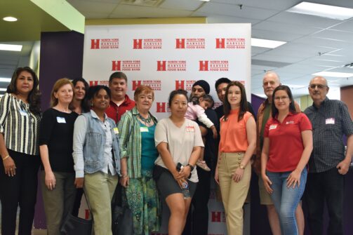 A dozen people stand for a group picture in front of a North York Harvest Food Bank backdrop.