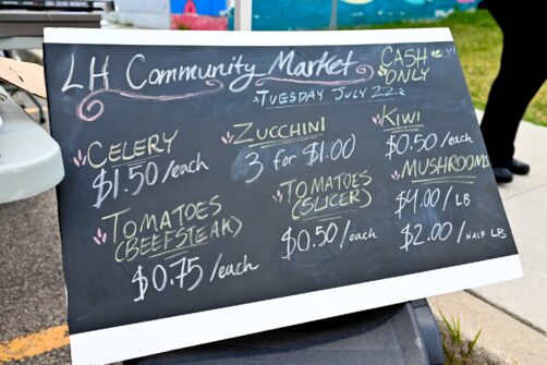A sign for the Lawrence Heights Green Market listing prices for various fruits and vegetables.