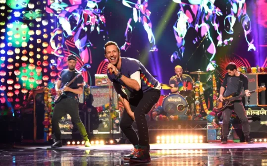 A live performance of the band Coldplay with colourful stage lights.