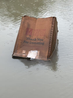 A North York Harvest Food Bank box floats in a giant puddle.
