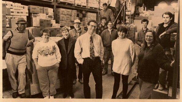 A sepia-toned photo from 1992 of the North York Harvest Food Bank team standing in a warehouse.