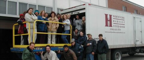 A group of people pose for a photo next to a red North York Harvest Food Bank truck.