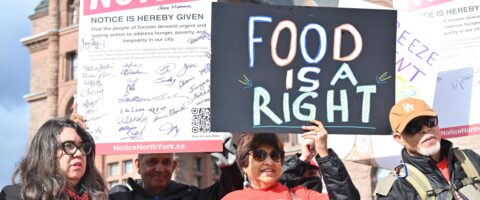 A person wearing a red North York Harvest Food Bank shirt holds a sign that reads Food if a right at an outdoor rally.
