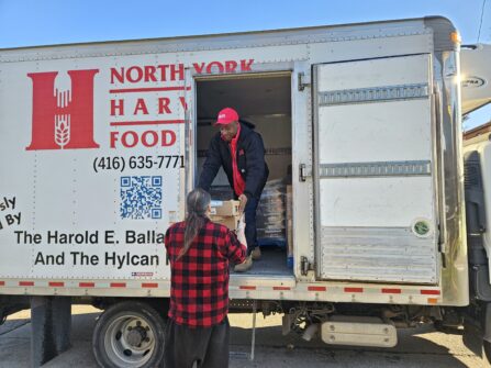 A person in a North York Harvest Food Bank delivery truck hands a box of food to a person standing on the ground.