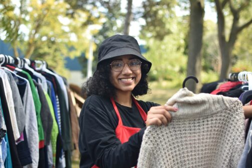 A person wearing a bucket hat holds out an article of clothing at an outdoor clothing bank event.