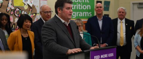 A man speaks at a podium that reads Feed More Kids during a press conference at a school in Toronto.