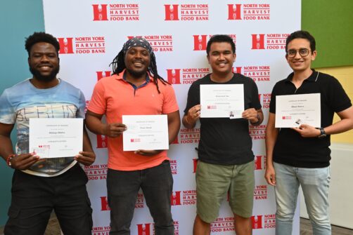 Four people hold graduation certificates and smile in front of a backdrop for North York Harvest Food Bank