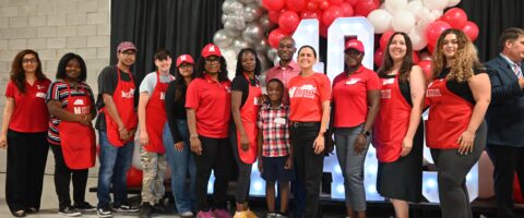 A large group of people wearing red North York Harvest Food Bank attire pose together in a warehouse with a large light-up '40' sign behind them.