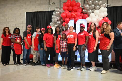A large group of people, of diverse cultures and ages, wearing North York Harvest Food Bank gear pose for a group picture in front of a large light-up 40 sign