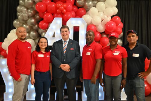 A group of people wearing red North York Harvest Food Bank attire stand in front of an LED sign that reads '40 Years' surrounded by balloons.