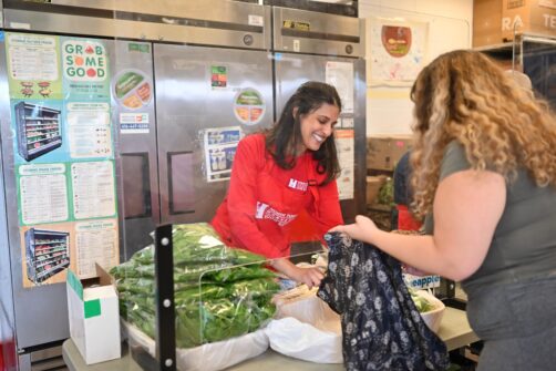 A woman in a red North York Harvest Food Bank shirt serves food to a client at a food bank in Toronto.