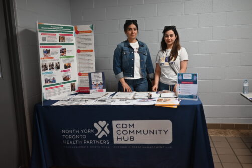 Two people stand at an information booth for healthcare services at Oriole Community Food Space.