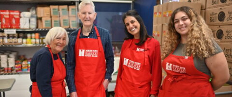 Four people wearing red North York Harvest Food Bank aprons smile in a food bank.
