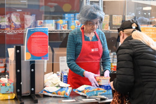 A woman in a red North York Harvest Food Bank apron serves food to a client.
