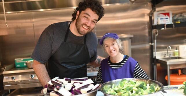 Two chefs stand in front of bowls of chopped eggplant and broccoli ahead of drop-in meal programming at Dixon Hall.