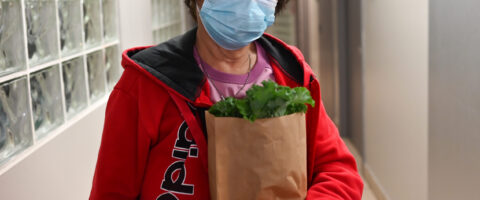 A woman holding a bag of fresh produce wears a mask and smiles at North York Harvest Food Bank