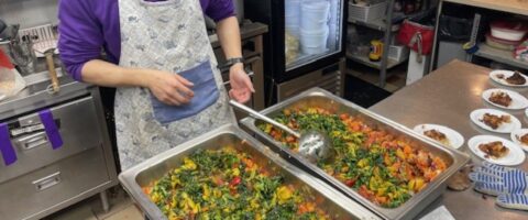 Trays of prepared food are being served onto individual plates at The Common Table in Toronto.