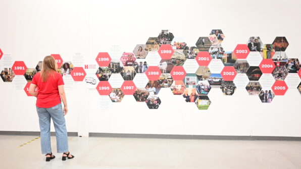 A person views a gallery wall with a timeline of North York Harvest Food Bank with interconnected honeycombs of both text and photos.