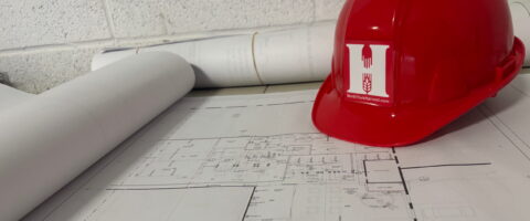 A hard hat with the North York Harvest Food Bank logo sits on paper blueprints in a warehouse.