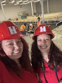 Two women wearing red North York Harvest Food Bank-branded hard hats smile at a Community Food Hub in Toronto.