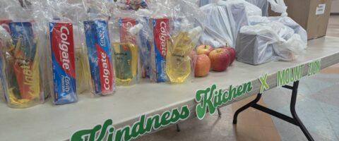 Care packages containing food and household items are arranged on a table with the words Kindness Kitchen & Mount Zion on it.
