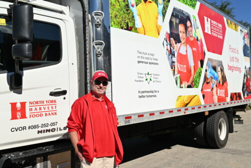 A person wearing red North York Harvest Food Bank attire stands next to a branded delivery truck.