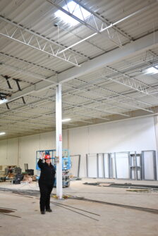 A person in a red North York Harvest Food Bank branded hardhat points above in a warehouse, where skylights are visible.