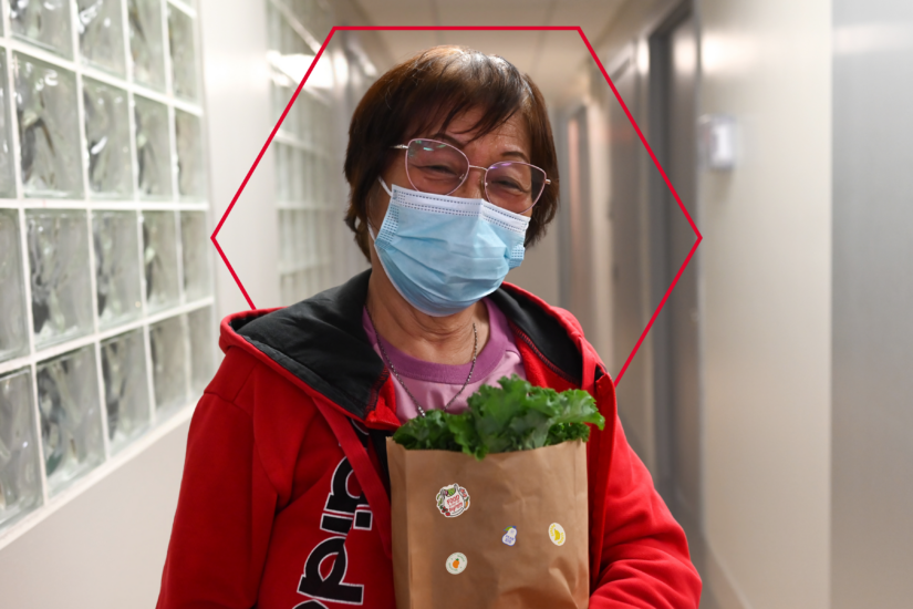 A woman holding a bag of fresh produce wears a mask and smiles at North York Harvest Food Bank