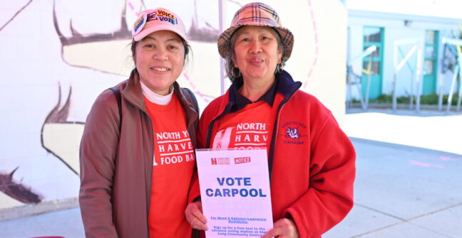 Two people wearing North York Harvest Food Bank clothing hold a sign that reads 'Vote Carpool' at an outdoor community fair.